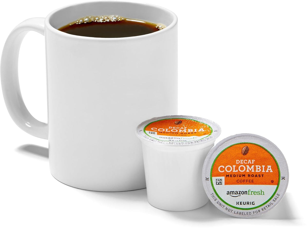 “White mug of coffee beside two AmazonFresh Decaf Colombia medium roast single-serve coffee pods with orange labels.”