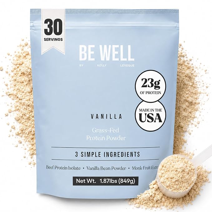 A light blue stand-up pouch of BE WELL Vanilla Grass-Fed Protein Powder, surrounded by spilled beige powder and a small scoop on a white background. The packaging features white and black text detailing 30 servings, 23g of protein, and Made in the USA.